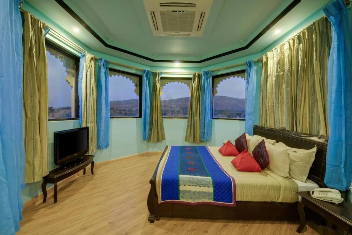 A room with a bed, a TV, a phone, and a window with curtains.