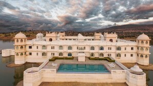 Un edificio grande y blanco de varios pisos, con una piscina central y múltiples balcones.