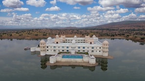A large, white, multi-story building with a central pool, surrounded by water and hills in the background.