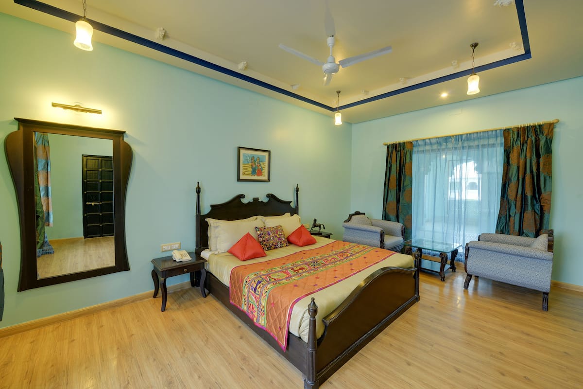 A bedroom with a bed, bedside table, nightstand, mirror, and a window with curtains.