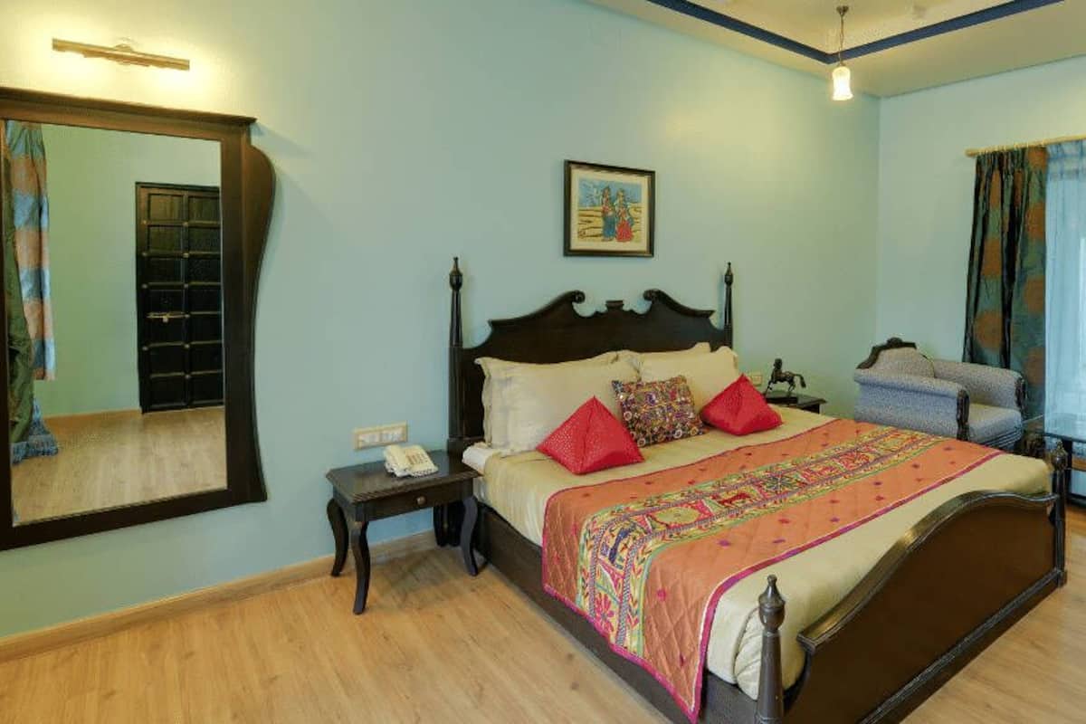 A bedroom with a large bed, bedside tables, a mirror, a chair, and a window with curtains.
