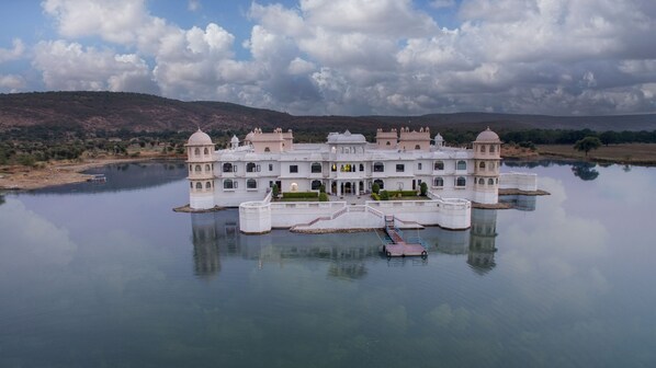 A large, white, multi-story building with a central courtyard, surrounded by water.