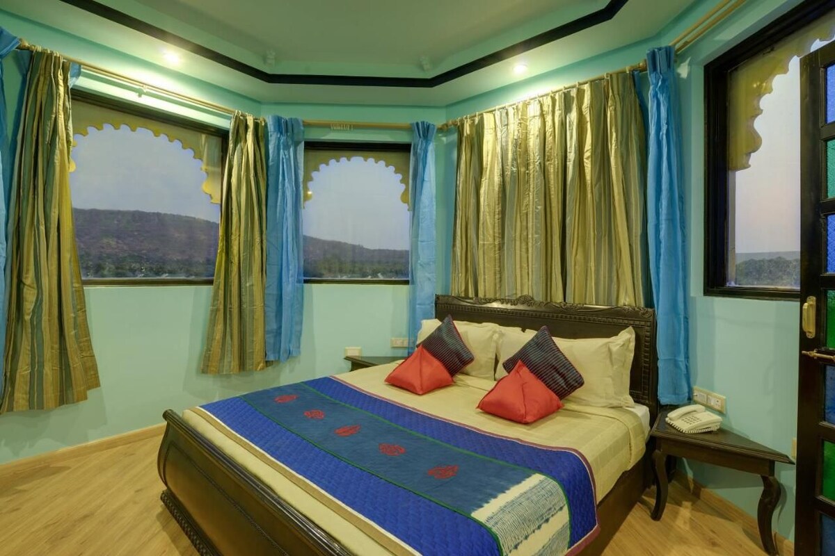 Una habitación con cama, cortinas, mesita de noche y vistas al exterior.