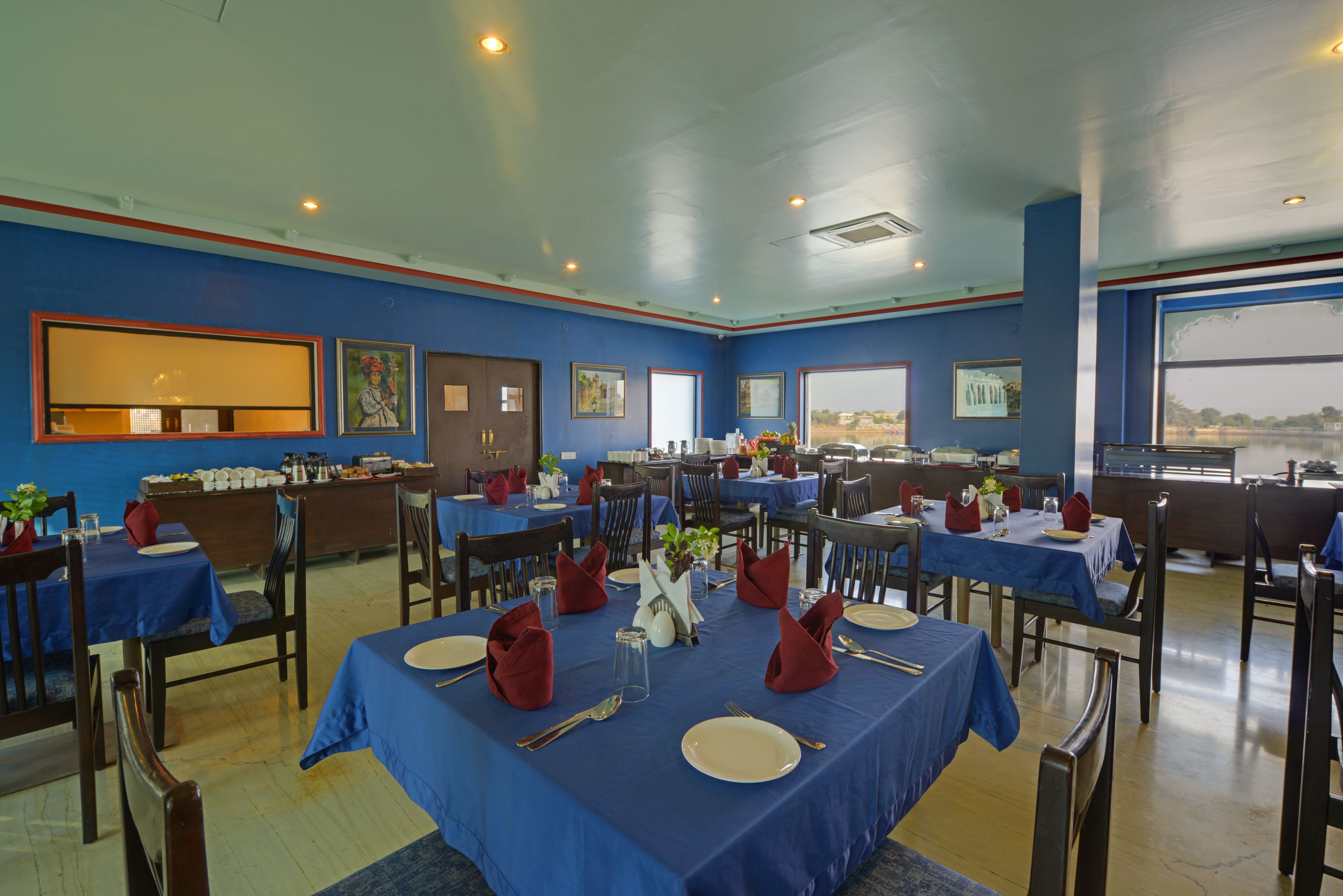 A restaurant with multiple tables set for dining, featuring blue tablecloths and red napkins.