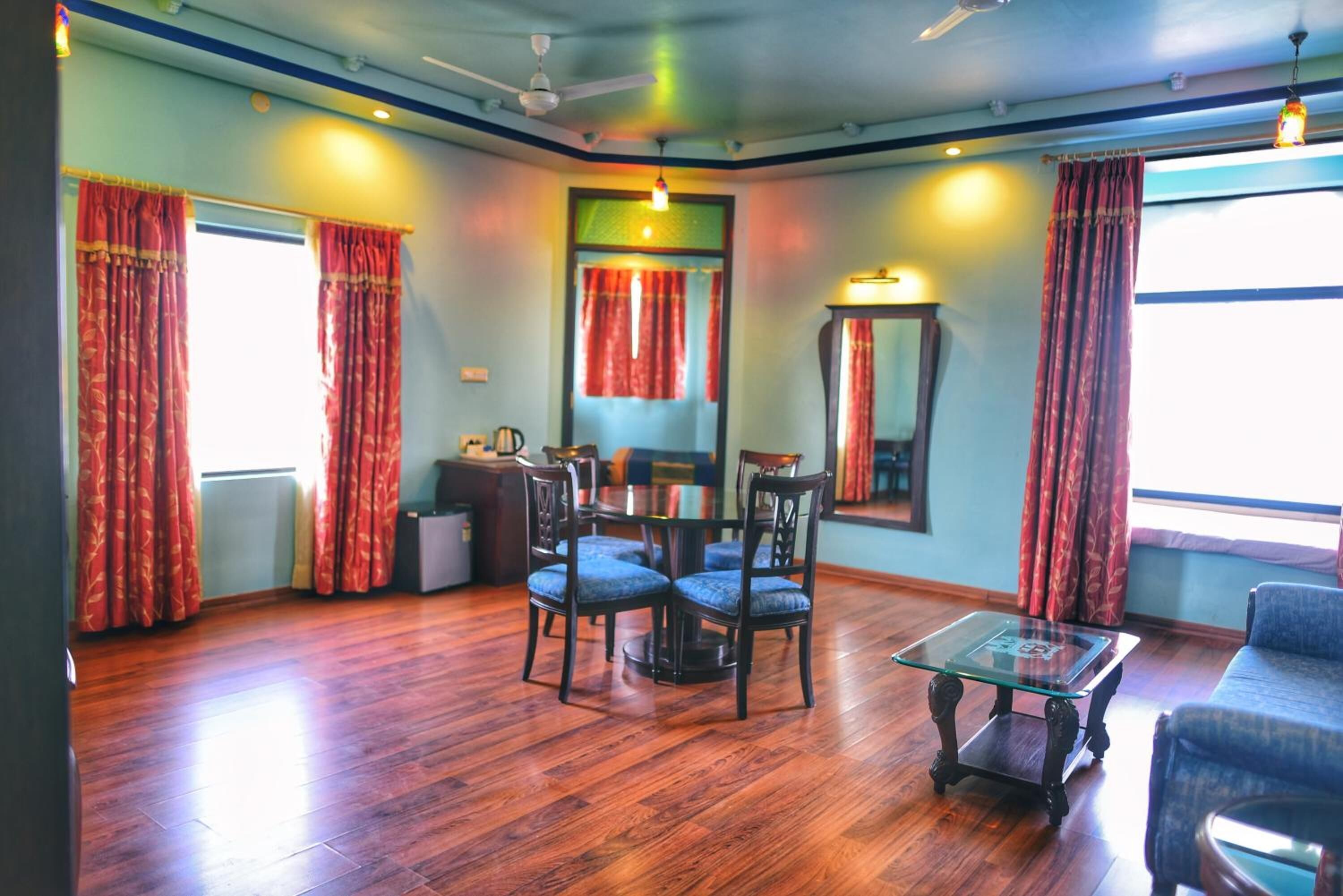 A room with a wooden floor, a glass coffee table, a dining table with chairs, and red curtains.