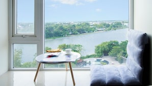Una habitación con un ventanal grande con vistas a un río, una mesa con una taza y un plato, y un sofá azul.