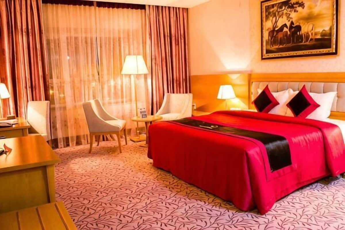 A hotel room with a large bed, two chairs, a desk, and a painting on the wall.
