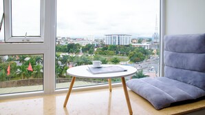 Una habitación con un ventanal grande, una mesa redonda con una taza y un libro, y un sofá gris.