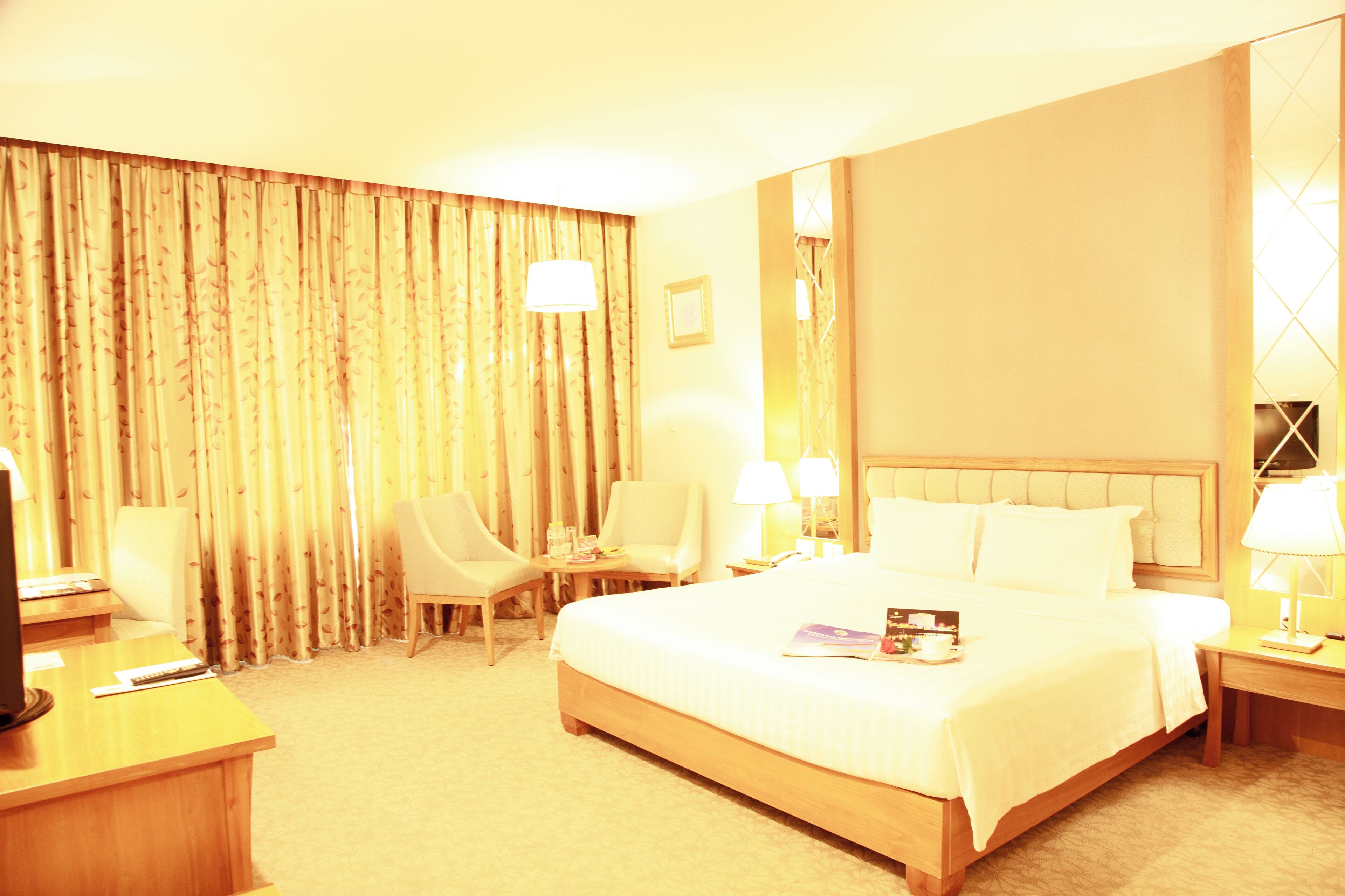 A hotel room with a large bed, two bedside tables, a desk with a chair, and a TV.