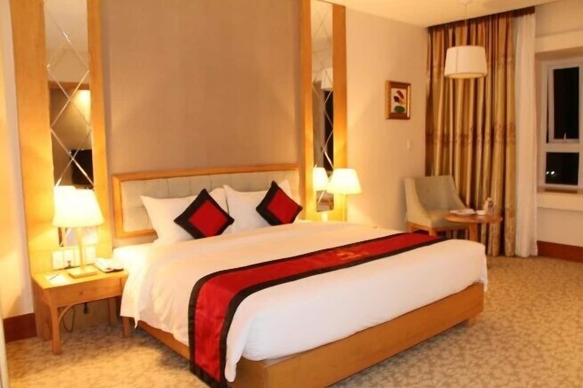 A hotel room with a large bed, bedside lamps, a chair, a small table, and a window with curtains.