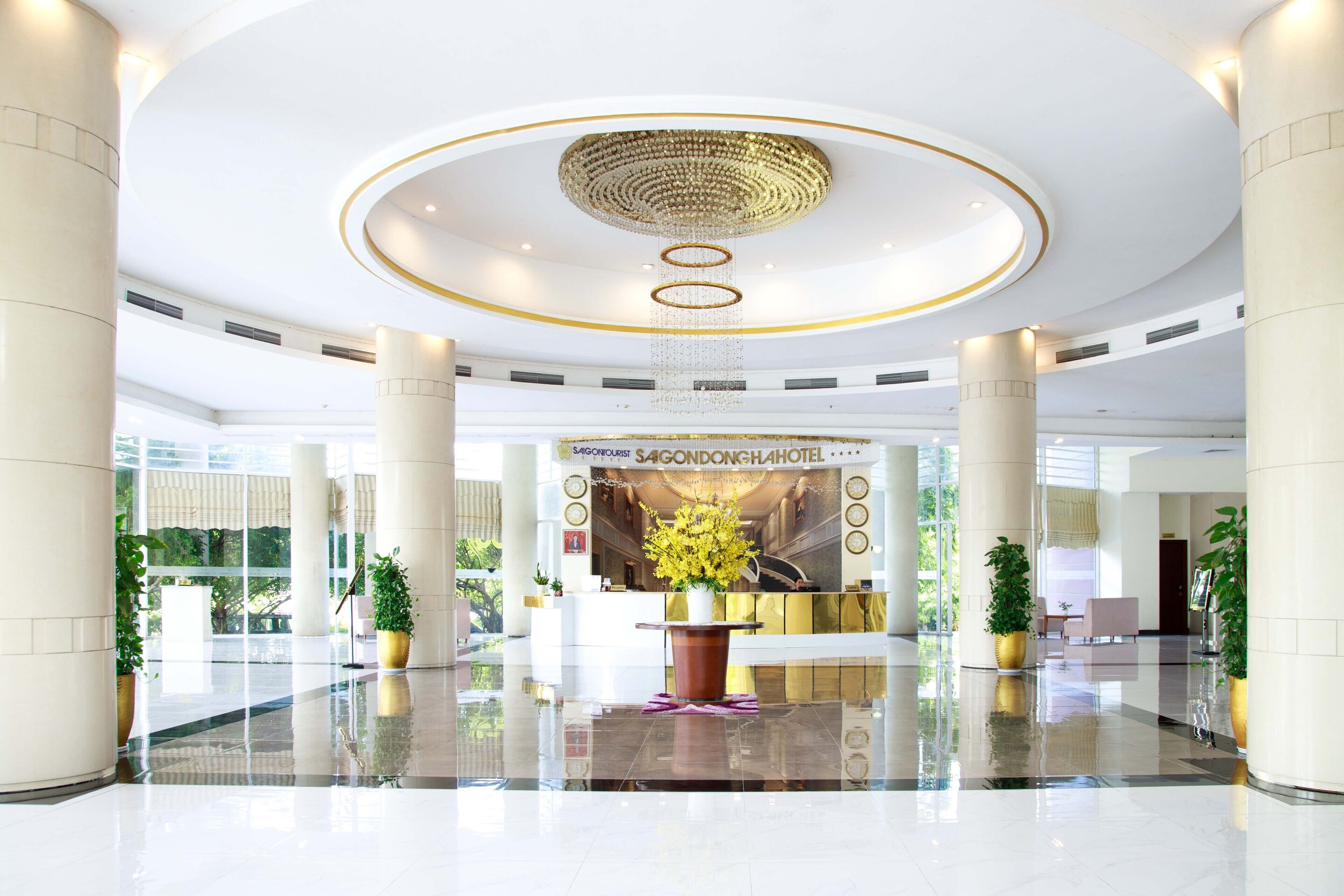 A spacious lobby with a reception desk, large columns, and a decorative chandelier.