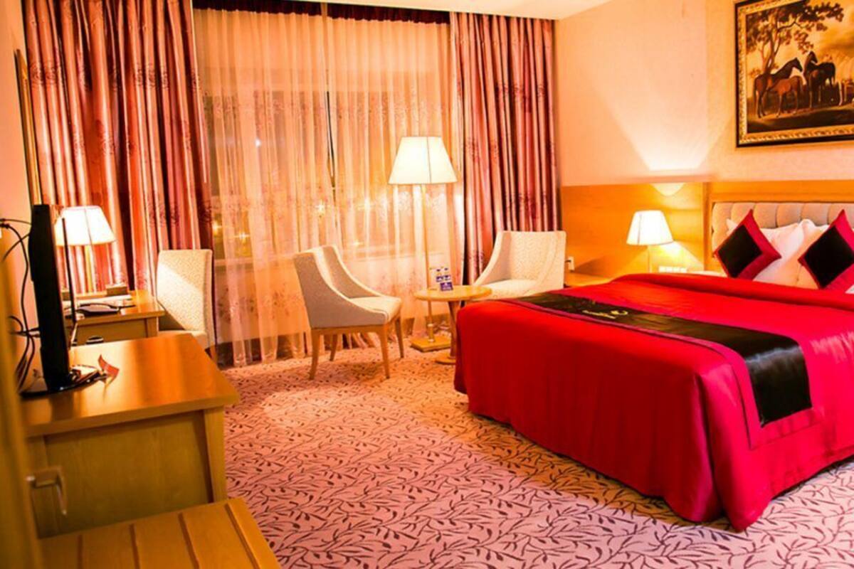 A hotel room with a large bed, two armchairs, a desk, and a television.