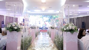 Un pasillo con suelo reflectante, bordeado por columnas con arreglos florales y adornos de cristal colgantes.