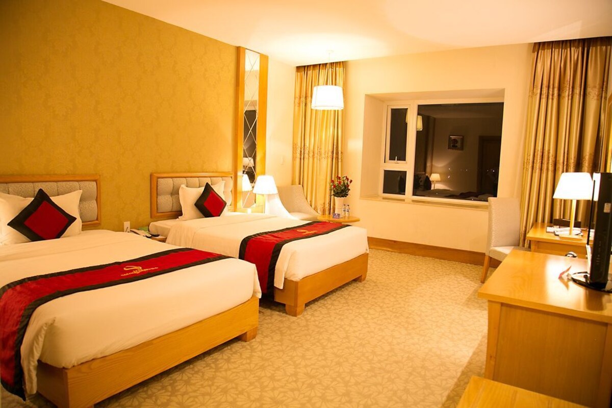A hotel room with two beds, a desk, a chair, a window, and a mirror.
