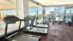 A gym with treadmills, stationary bikes, and a pool visible through large windows. - Ramada by Wyndham Tekirdag (Tekirdag)
