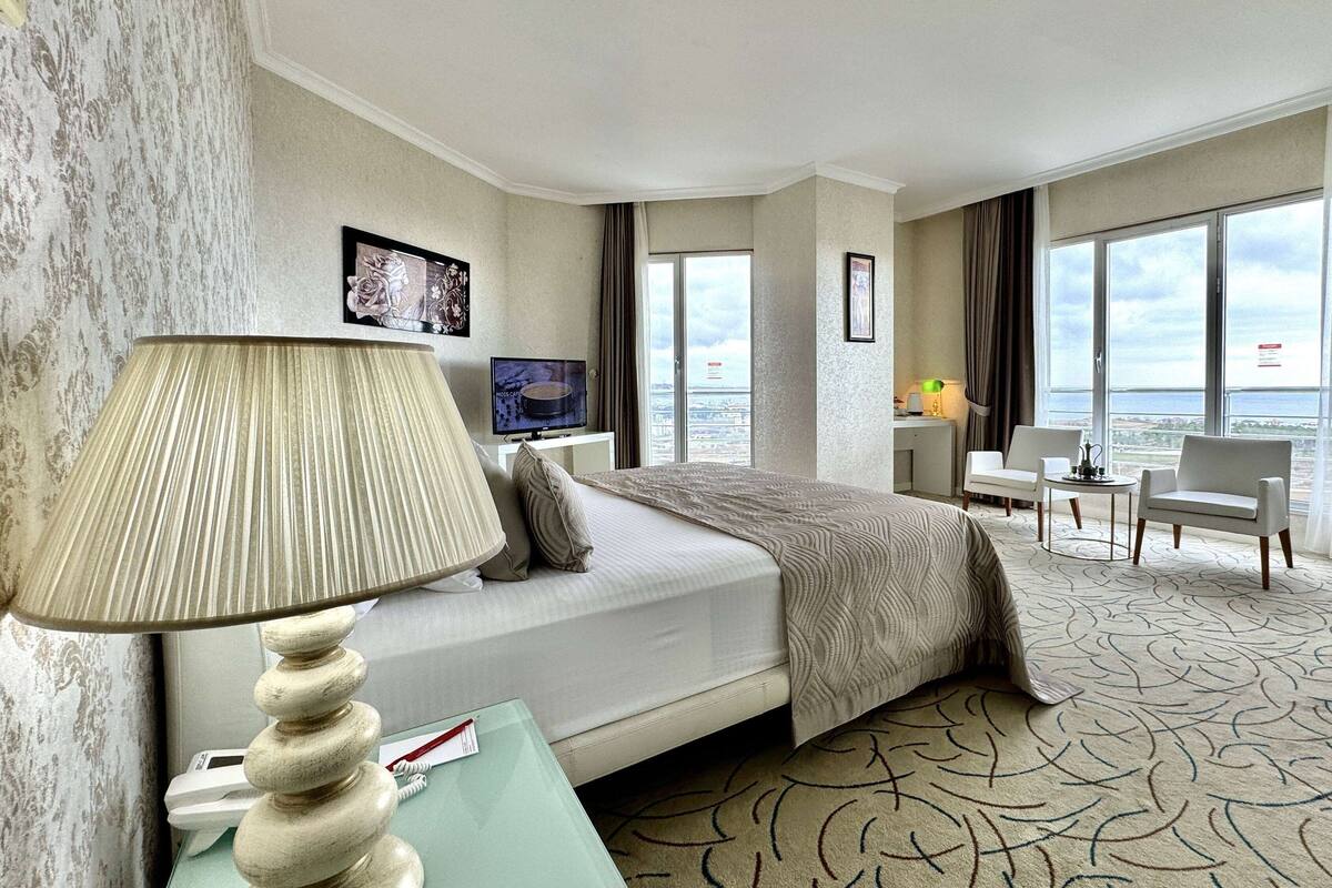A hotel room with a bed, a TV, a desk, and a view of the city.