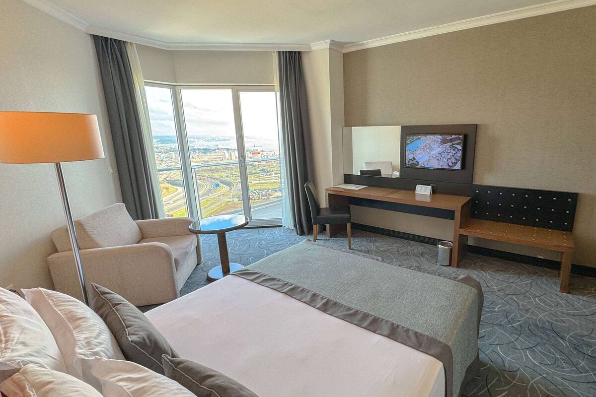 A hotel room with a bed, a desk, a TV, a sofa, and a view of a cityscape.