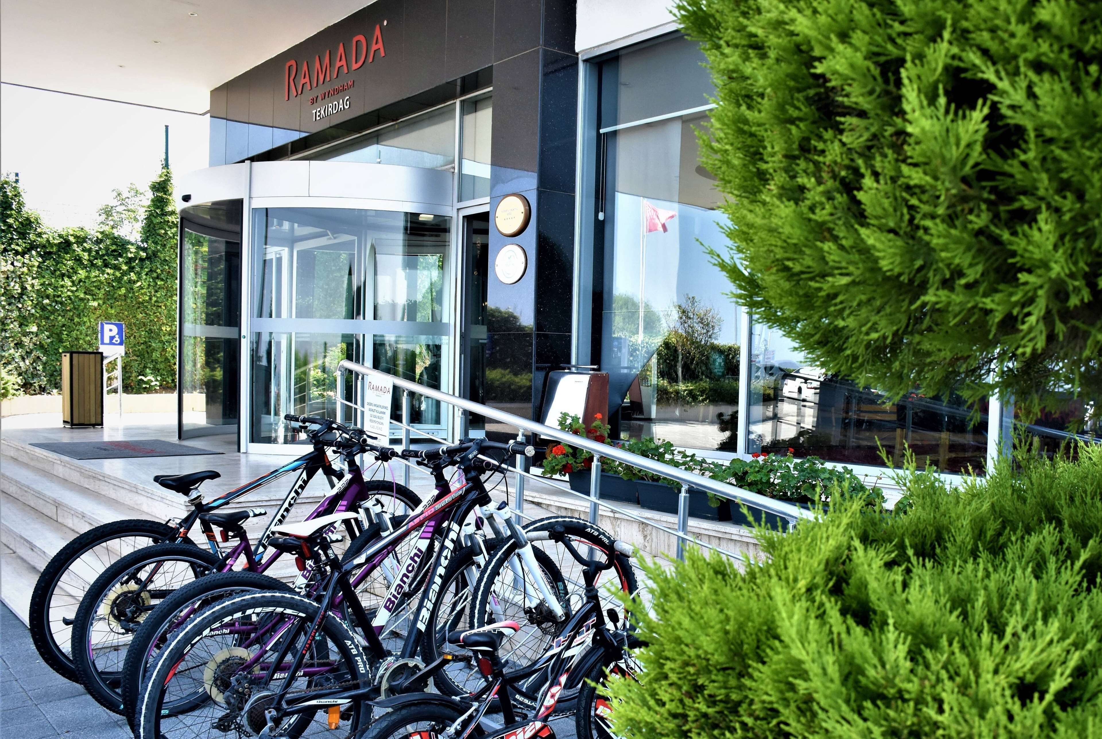 En moderne bygning med glasefterdør, et skilt med teksten “RAMADA” og flere cykler parkeret udenfor.