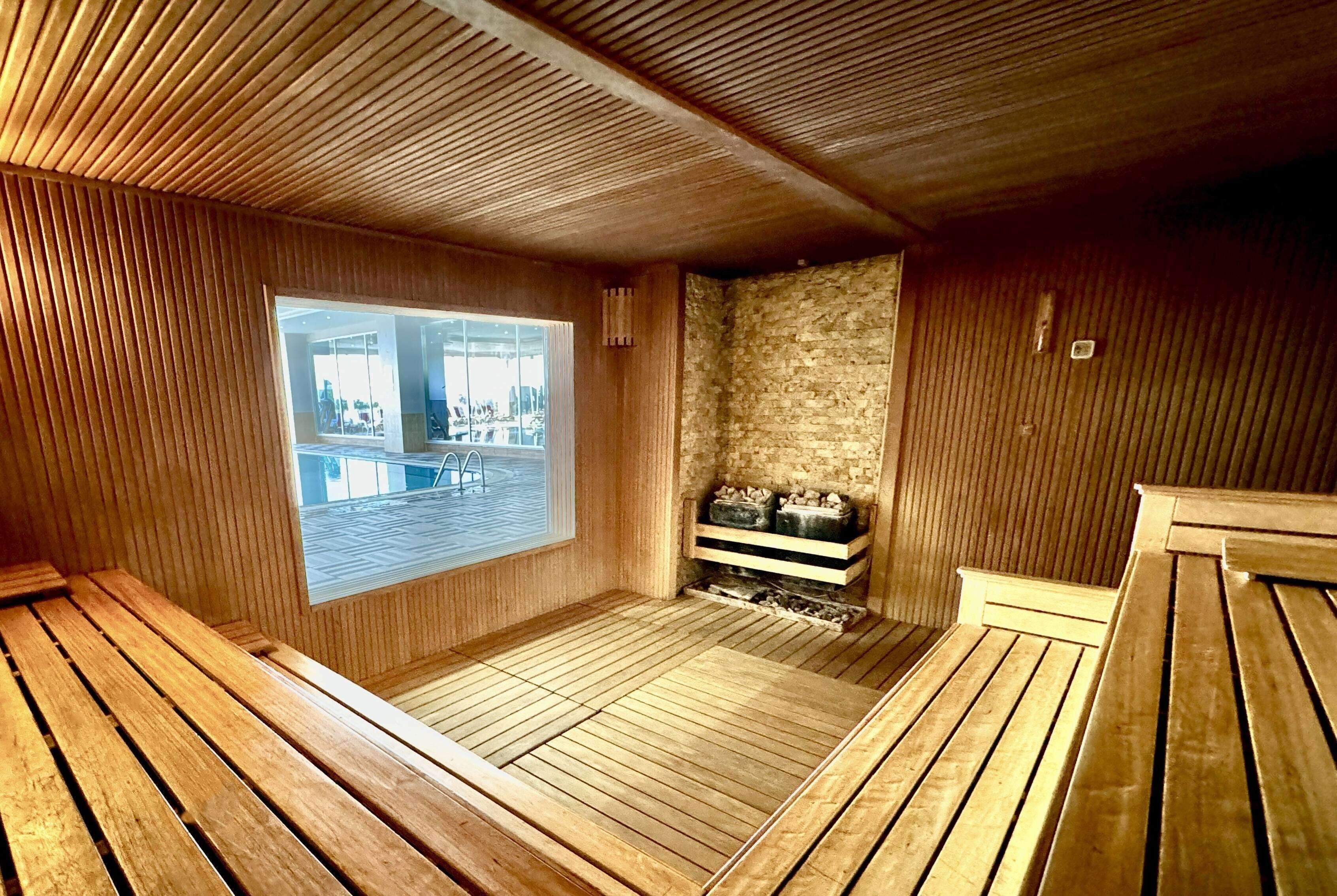 Un sauna con bancos de madera, pared de piedra y ventana con vistas al exterior.