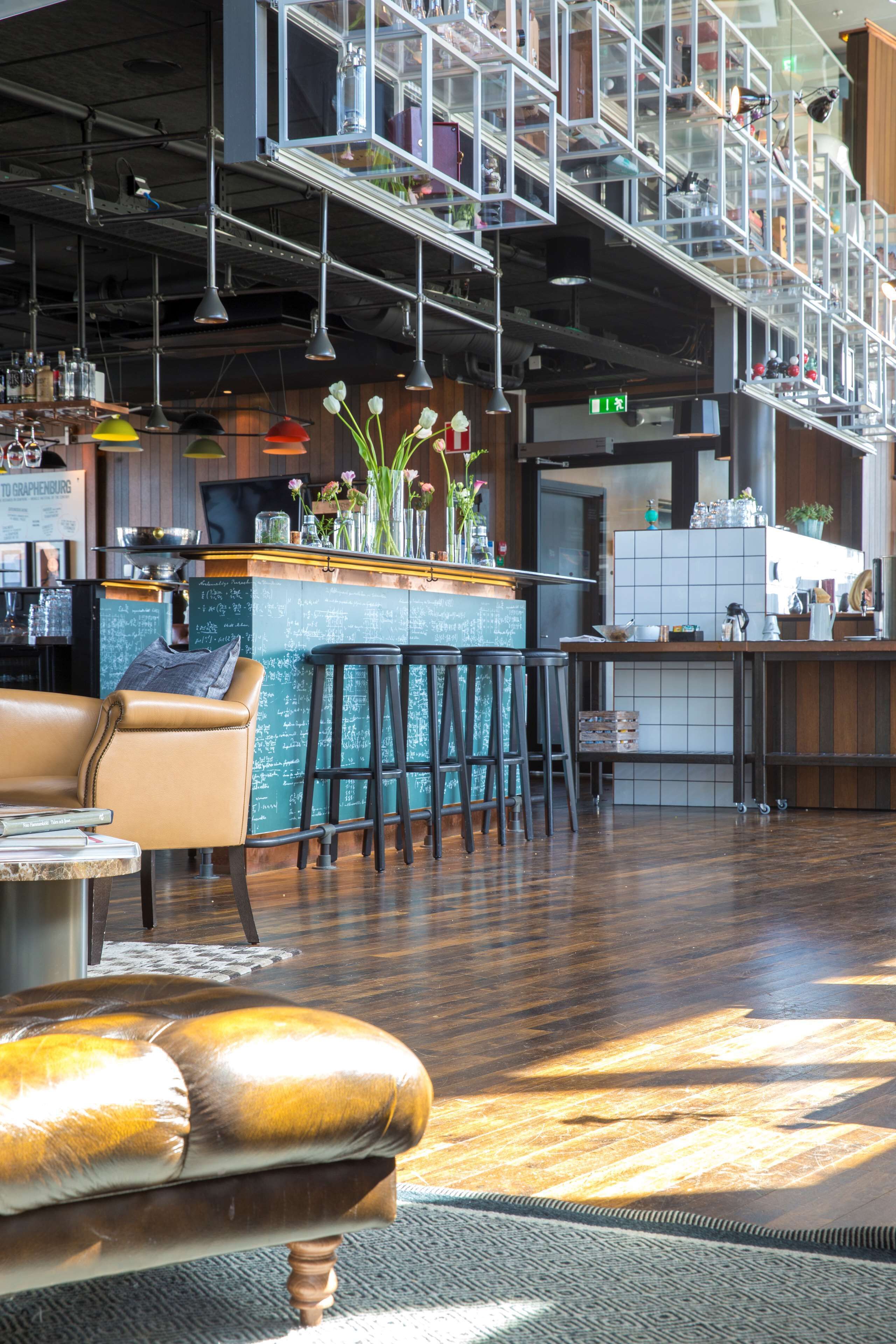 En modern bardel med högt i tak, synliga ventilationskanaler och ett stort utbud av barstolar.