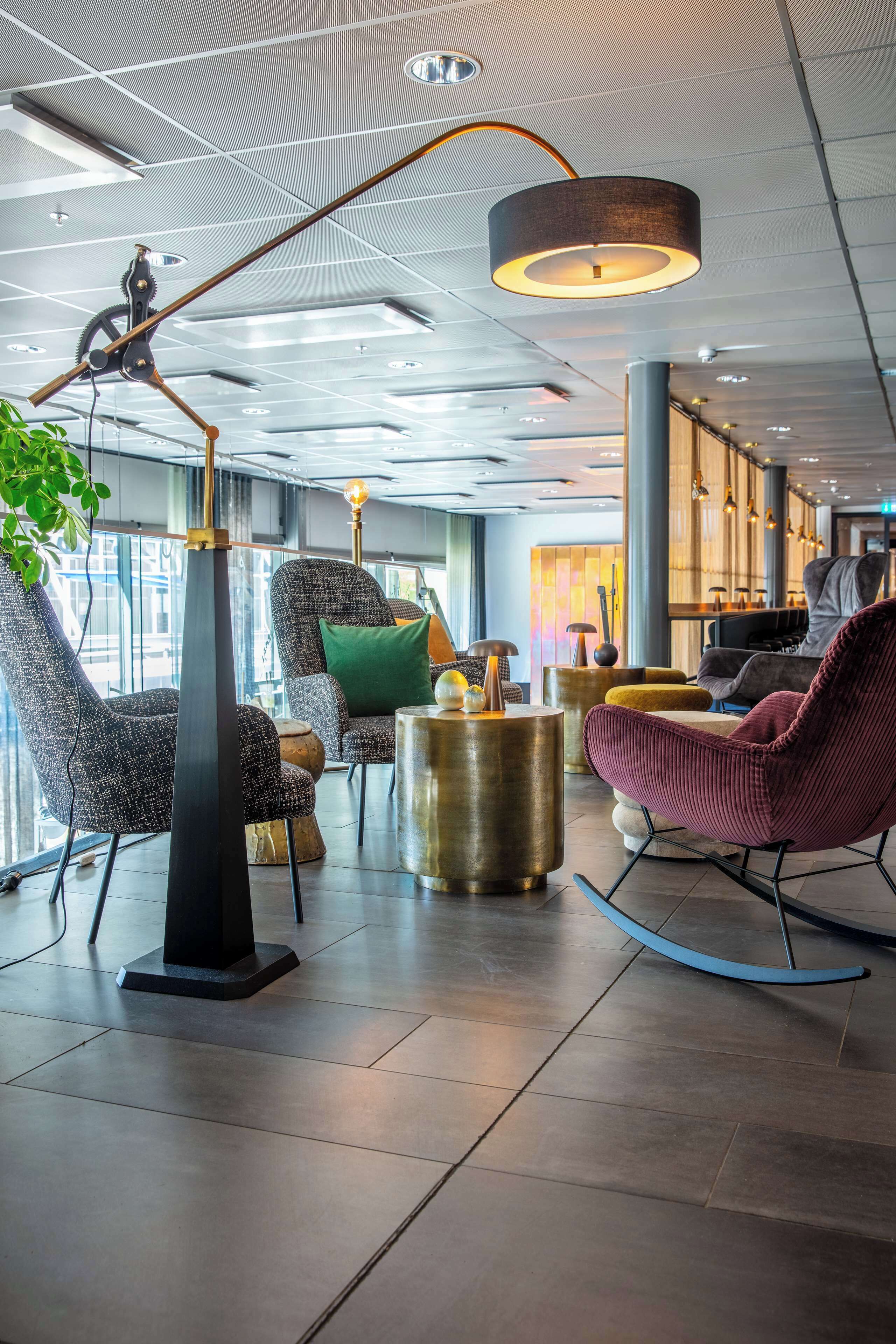 Un espace de détente moderne, doté de meubles contemporains, d’une grande plante et d’un plafond orné d’un motif en réseau.