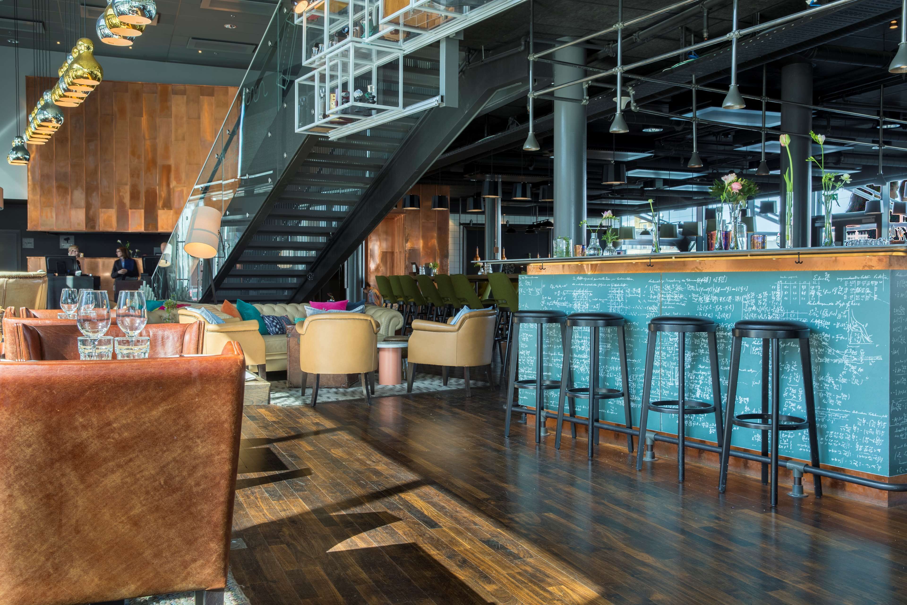 A modern bar area with wooden flooring, bar stools, and a chalkboard menu.
