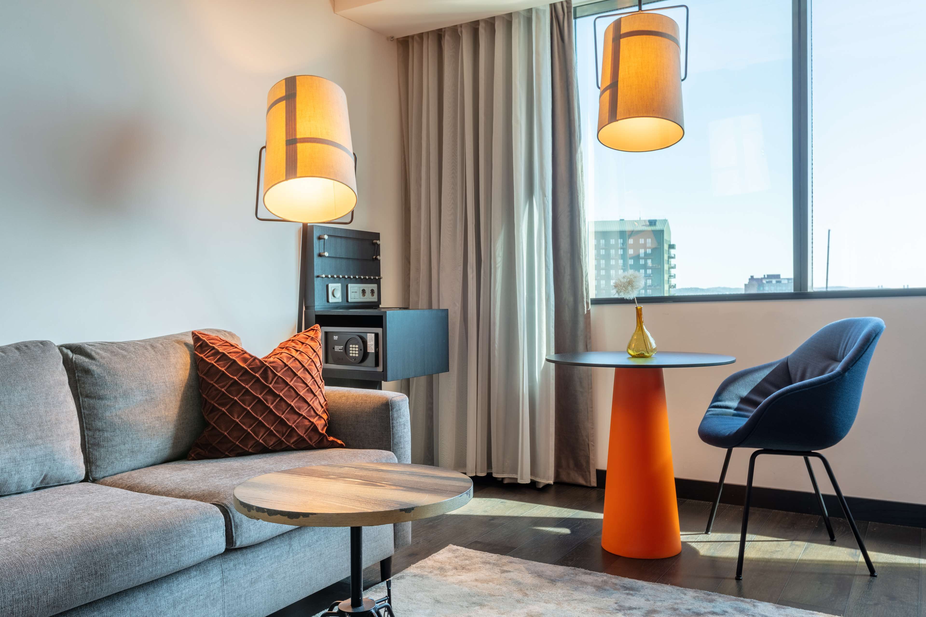 Un salon moderne avec un canapé gris, une table basse ronde, un fauteuil bleu et deux lampes suspendues.