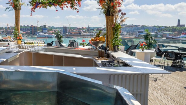 En bar på taket med en pool, sittplatser och utsikt över staden.
