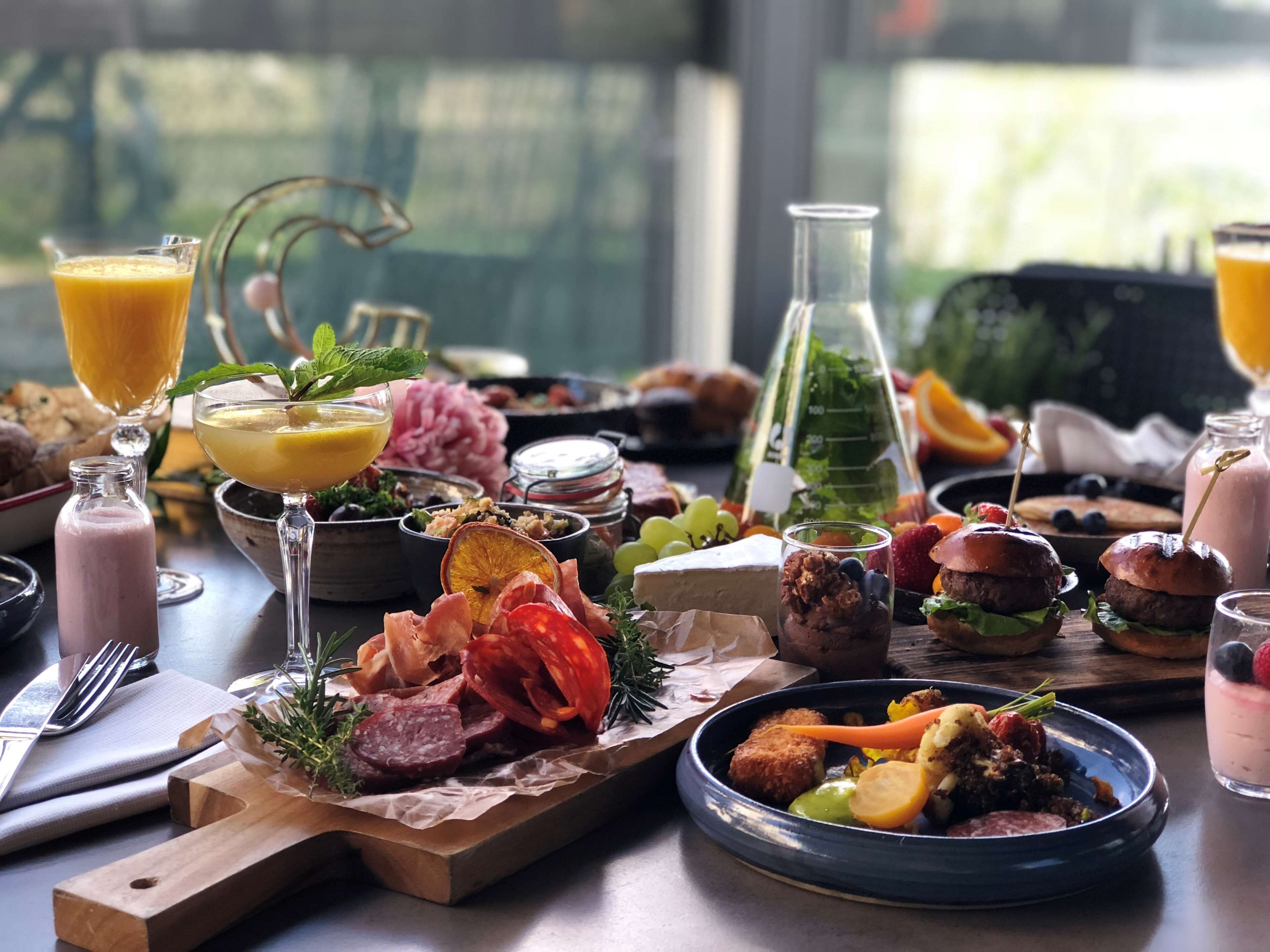 A breakfast buffet with various food items, drinks, and a large window in the background.