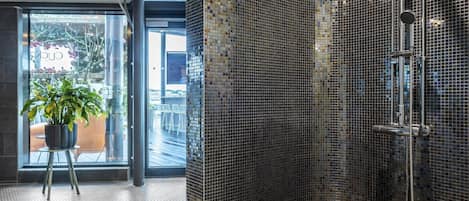 A modern bathroom with a glass shower enclosure, a potted plant, and a view of the outdoors.