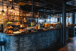 A bar area with a chalkboard menu, shelves with bottles, and a variety of fruits and condiments.