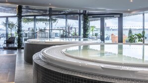 A modern indoor swimming pool with glass walls, a tiled floor, and potted plants.
