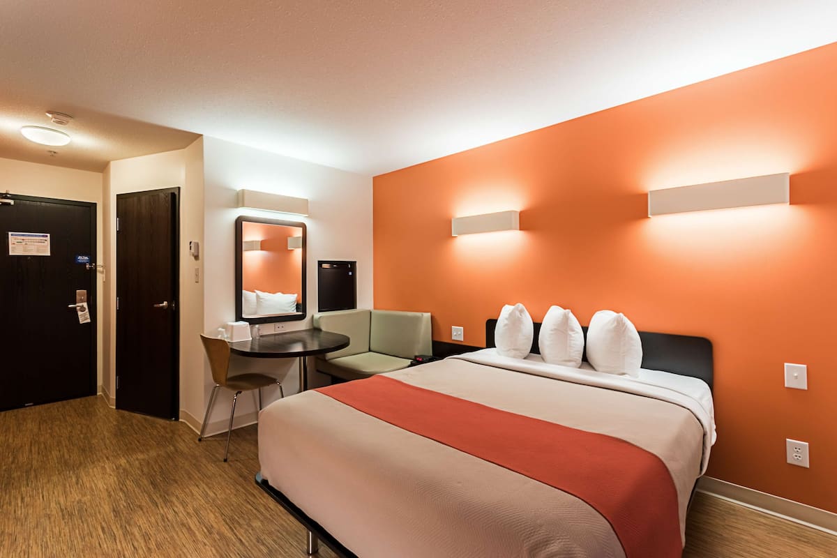 A hotel room with a bed, a desk, a chair, and a small table.