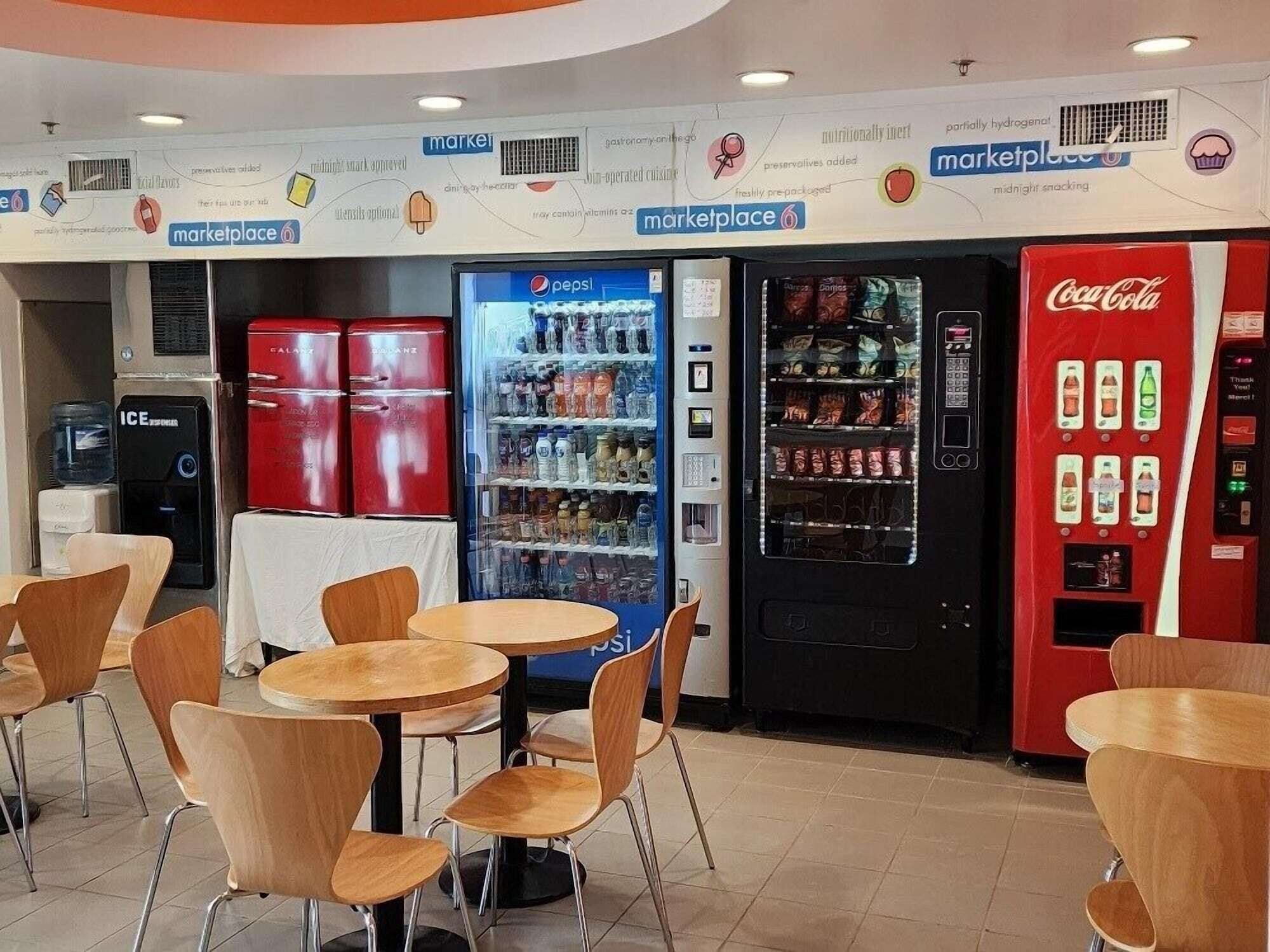 Un patio de comidas con máquinas expendedoras, incluyendo Pepsi y Coca-Cola, y un dispensador de agua.