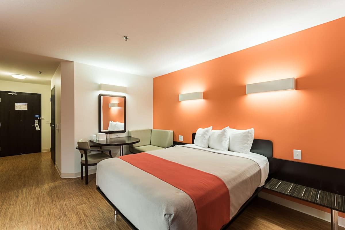 A hotel room with a bed, a desk, and a chair. There is a door and a sign on the wall.
