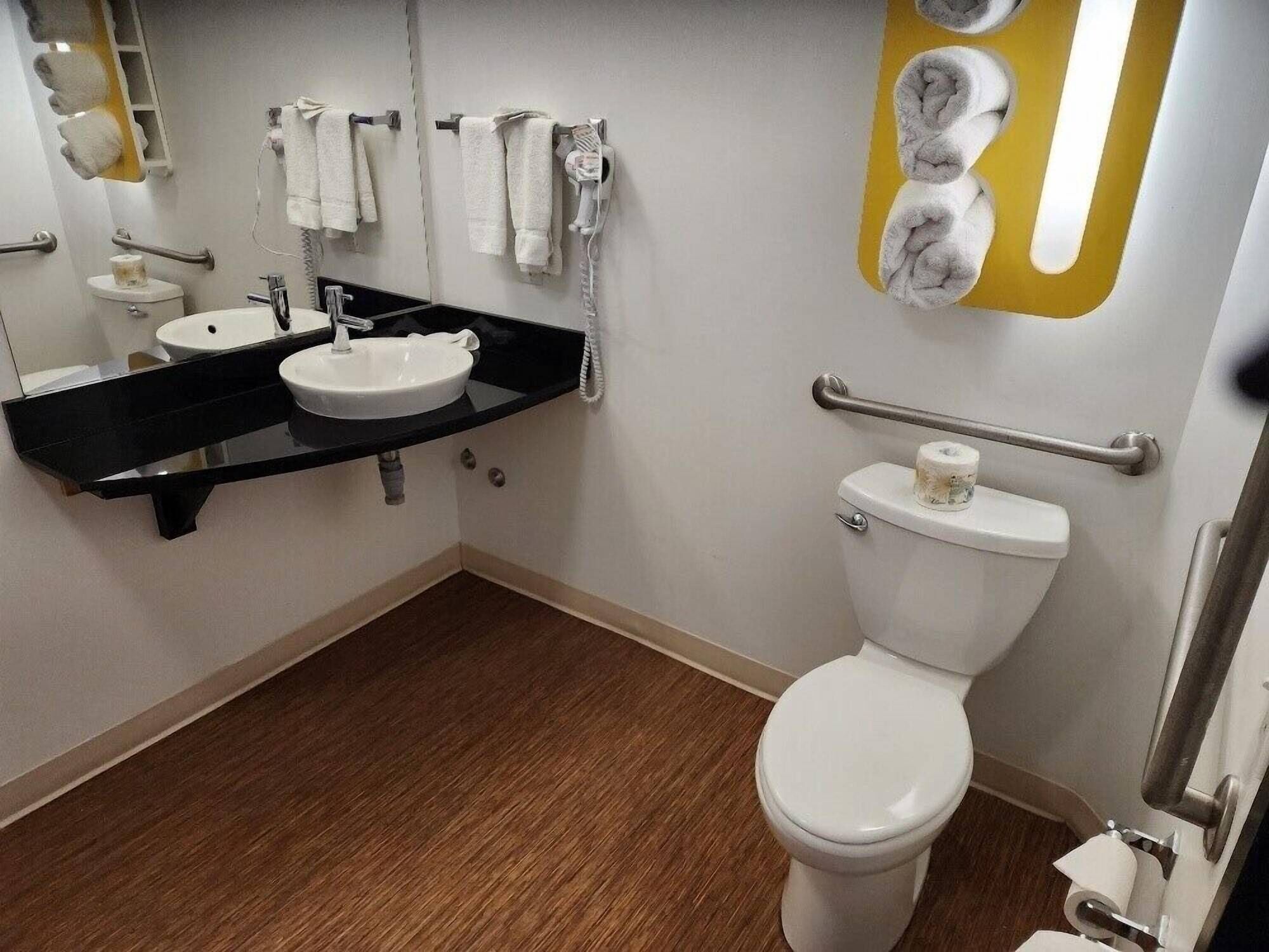 A bathroom with a white toilet, a sink, and a mirror. There are towels hanging on a rack and a hairdryer on the wall.