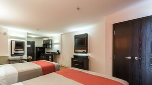Habitación de hotel con dos camas, un escritorio, una silla, televisión, armario y espejo.