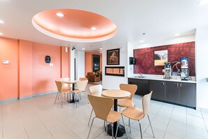 A modern interior with round tables and chairs, a kitchen area with appliances, and artwork on the walls. - Motel 6 Moosomin, SK (Moosomin)