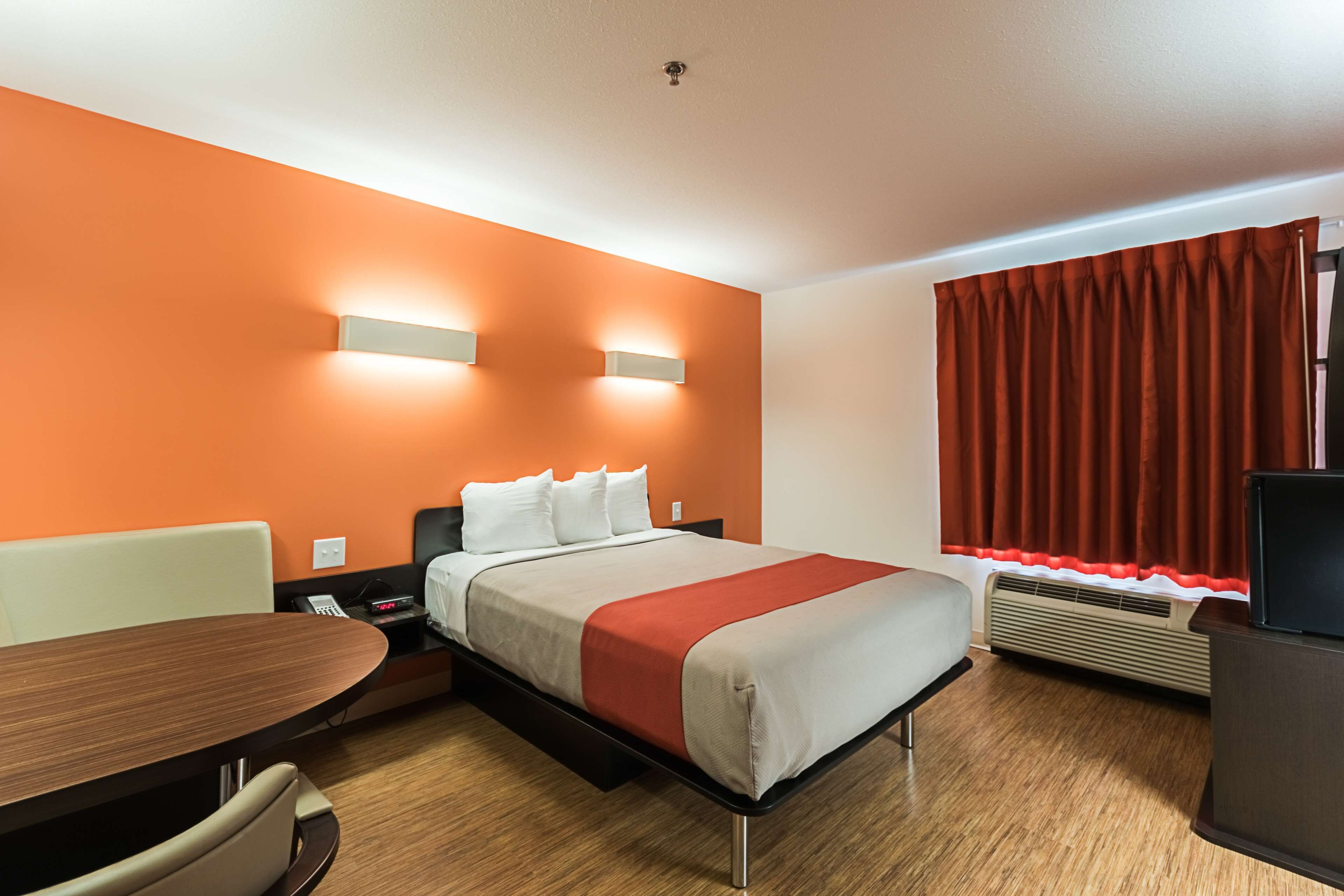A hotel room with a bed, a desk, a chair, a heater, and a window with curtains.