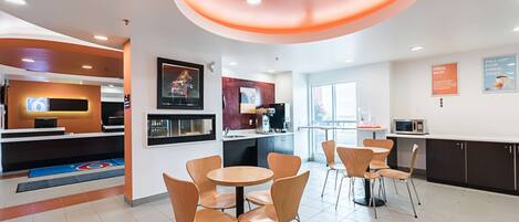 Un restaurante moderno con mesas redondas y sillas naranja, una zona de cocina y una barra con máquina de café.