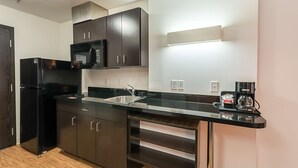 Una cocina compacta con armarios oscuros, un refrigerador negro, un microondas, un lavamanos y una cafetera.