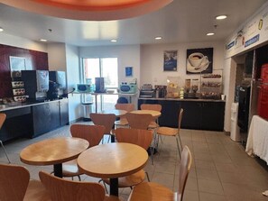 A café with round tables and chairs, a counter with coffee machines, and a refrigerator. - Motel 6 Moosomin, SK (Moosomin)