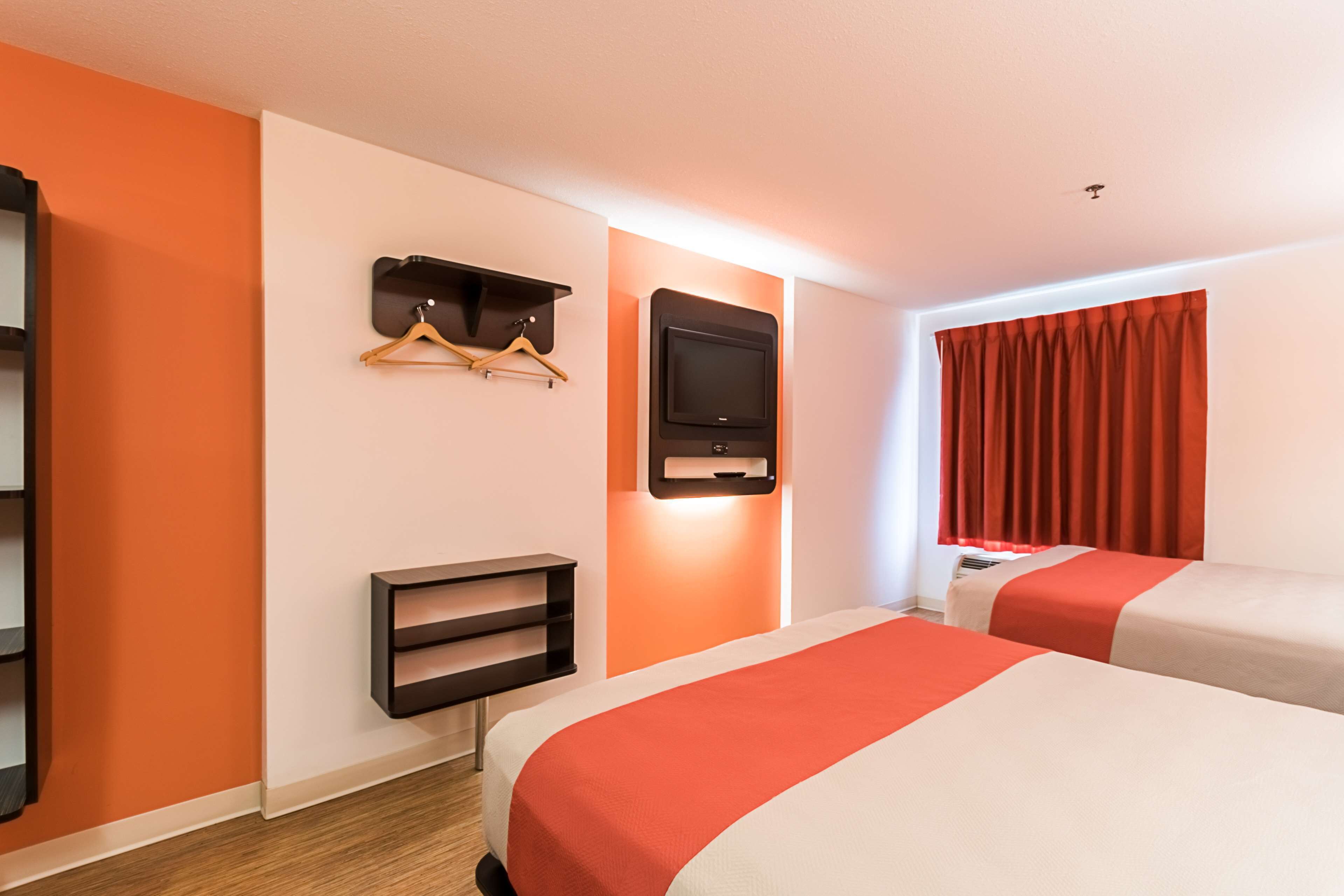 Een hotelkamer met twee bedden, een televisie, een kapstok en een plank.