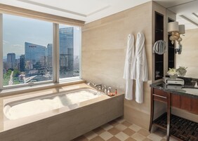 A modern bathroom with a large bathtub, a vanity with a mirror, and a view of a cityscape through a large window.