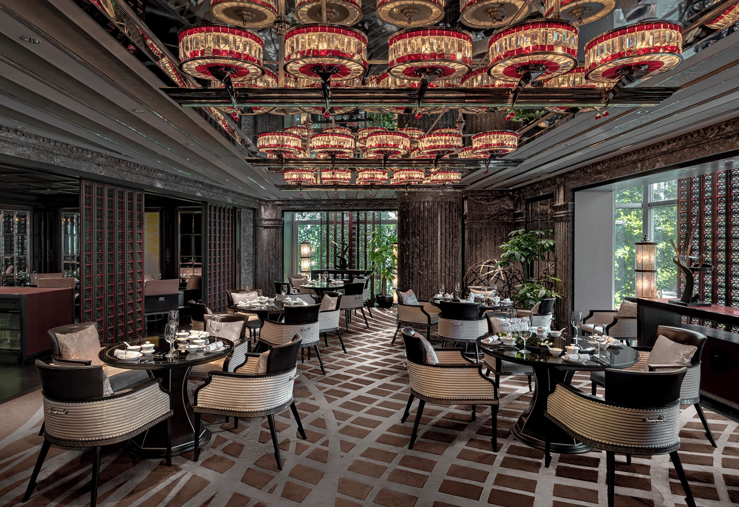 A luxurious dining area with multiple tables and chairs, ornate chandeliers, and a patterned floor.