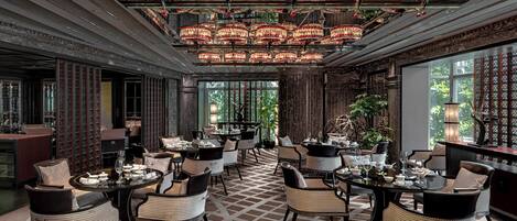 A luxurious dining area with multiple tables and chairs, ornate chandeliers, and a patterned floor.
