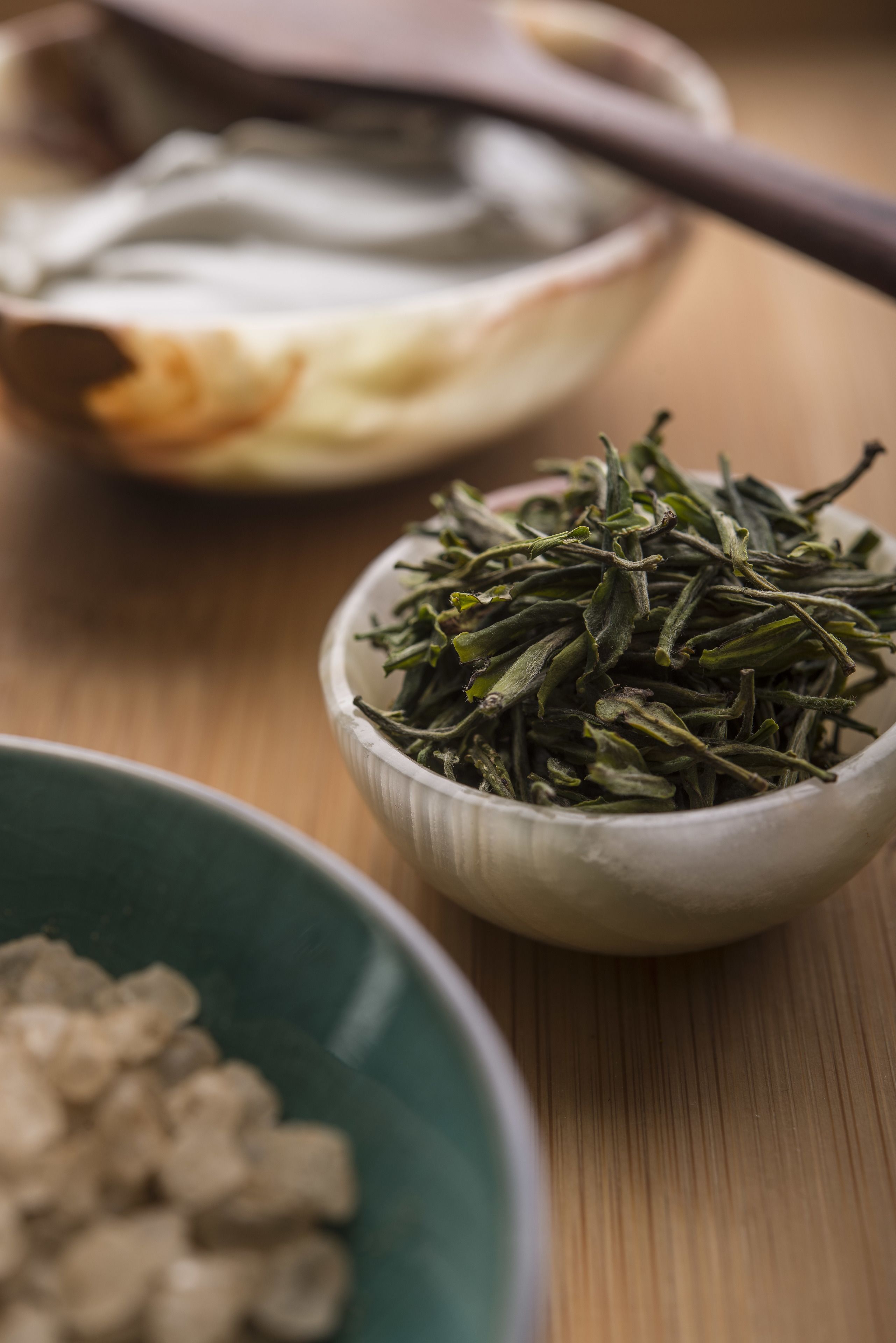 A wooden table with a bowl of dried herbs and a spoon.