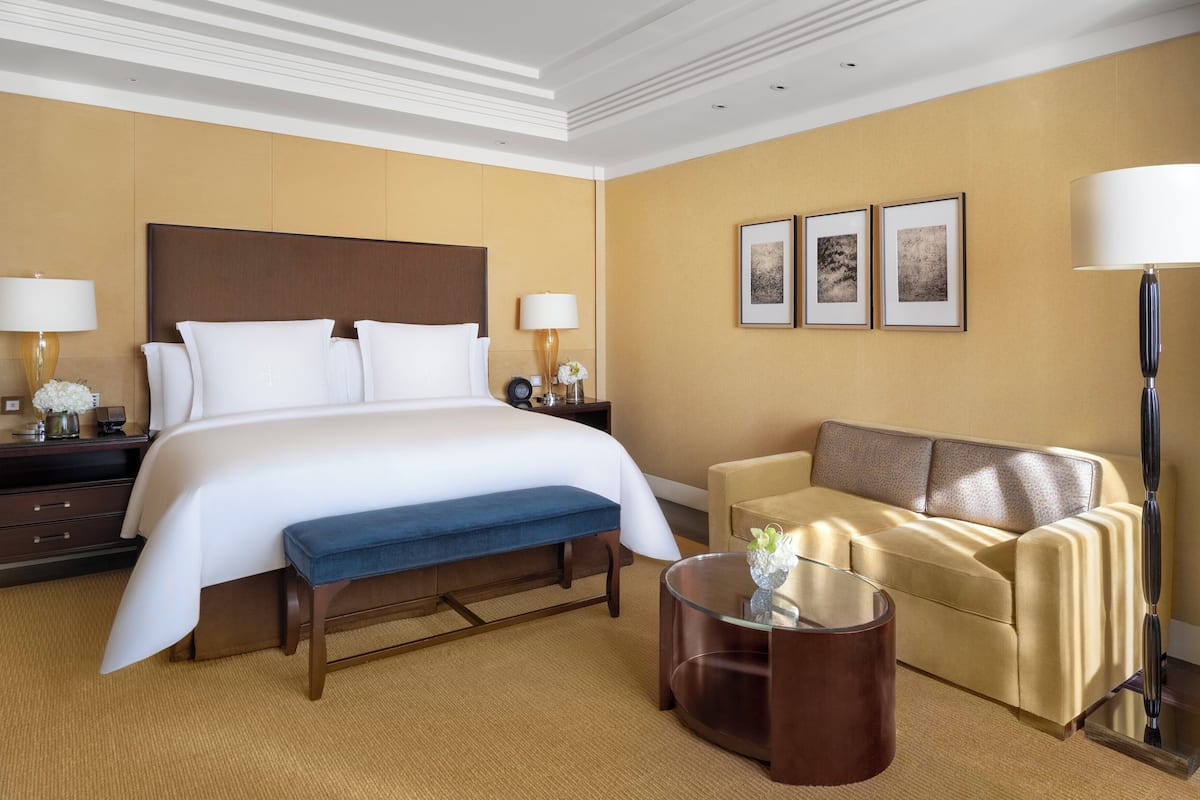 A hotel room with a large bed, a sofa, a coffee table, and a lamp.