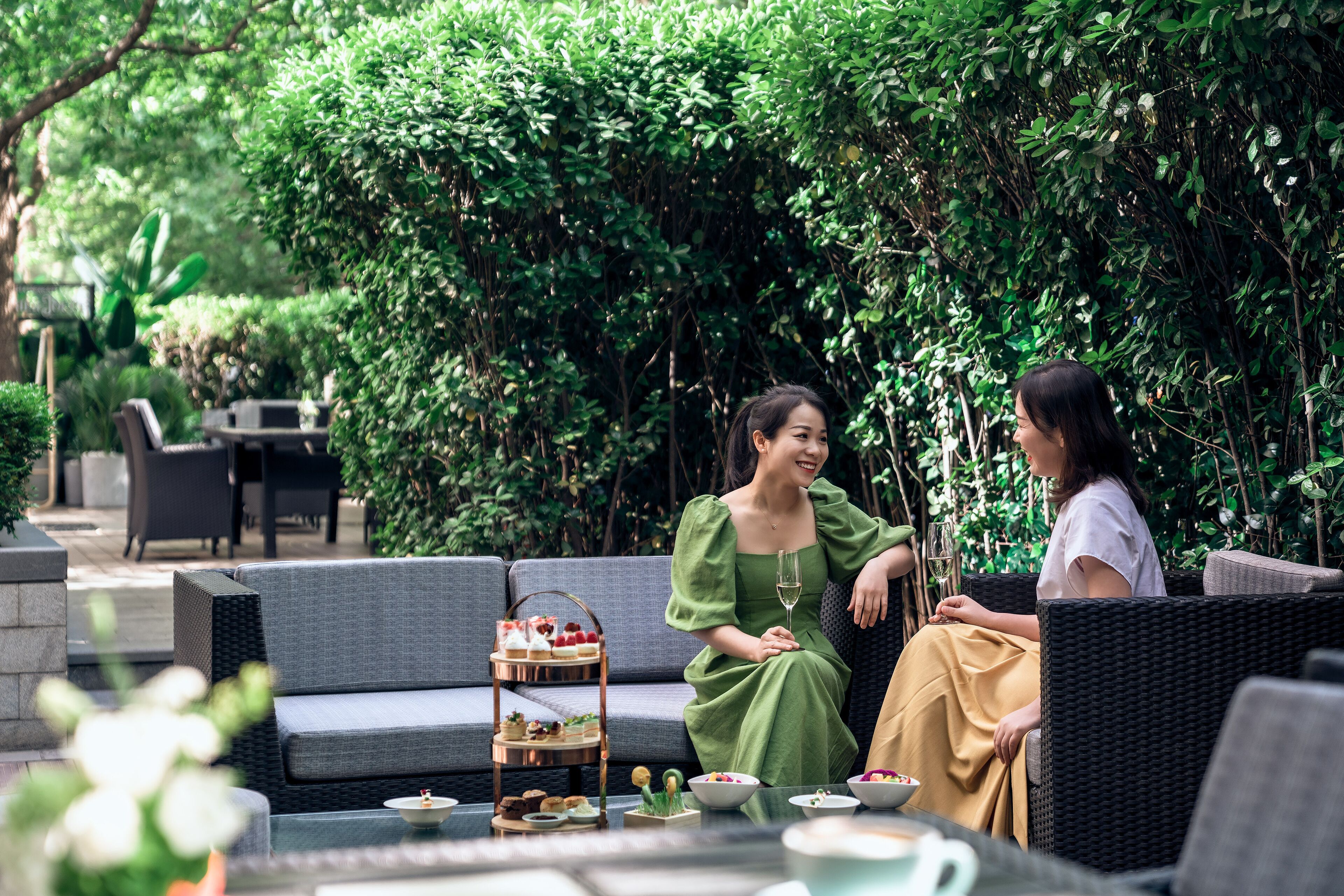 An outdoor seating area with wicker furniture, a tiered dessert cart, and lush greenery in the background.