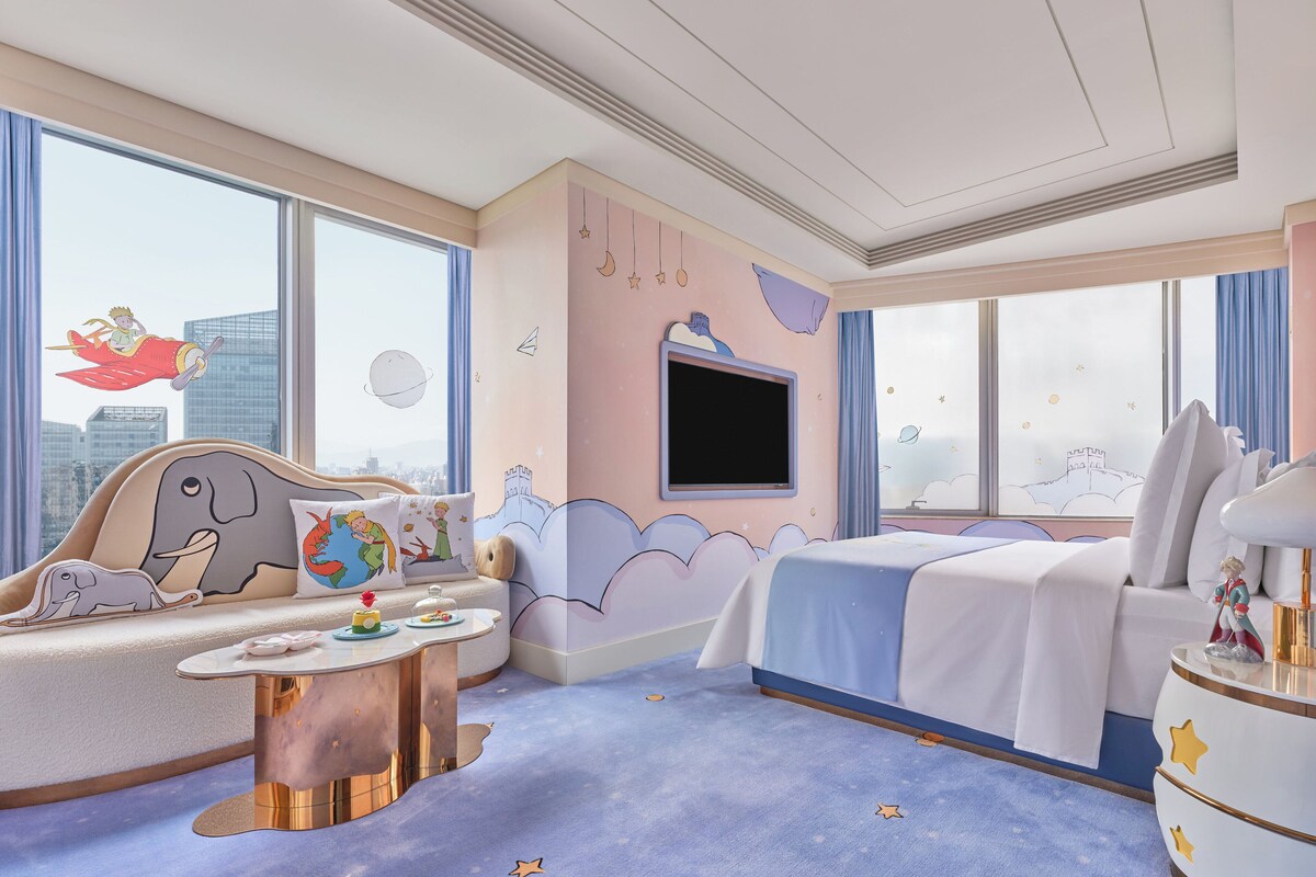 Ein Kinderzimmer mit Blick auf die Stadt, inklusive Sofa, Bett, Fernseher und Nachttisch.